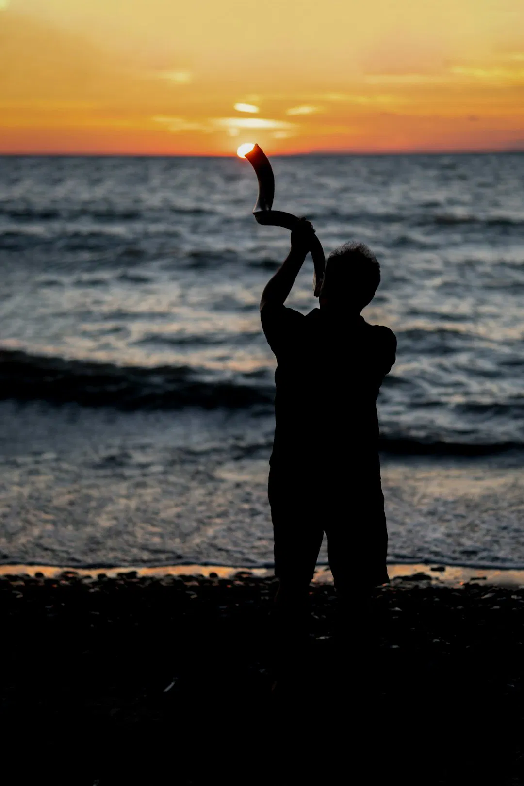Man in silhouette playing a shofar during sunset on Lake Erie